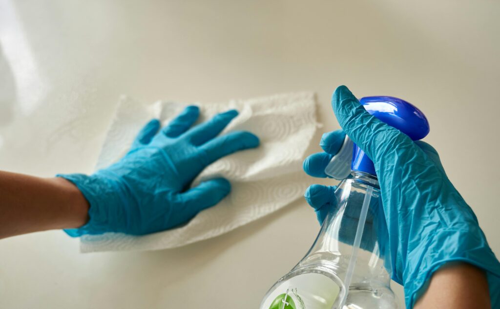 Close-up of gloved hands using disinfectant spray and cloth for cleaning surface.